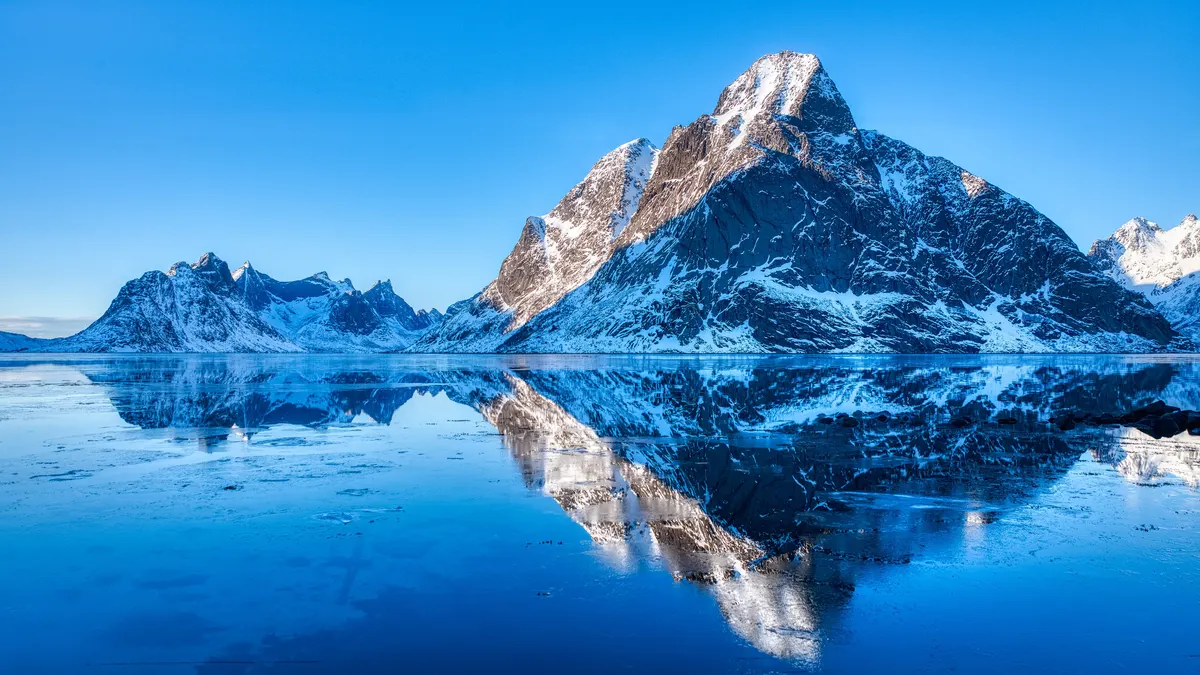 Snow-covered mountain reflected in a still fjord